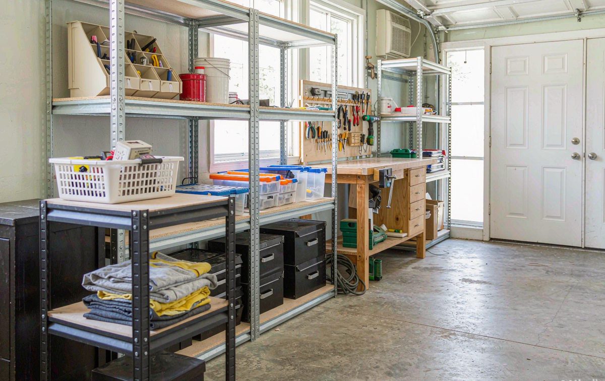 Slotted angle steel shelving fitted along a garage wall holding toolboxes and storage bins